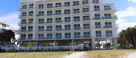 A multi-story hotel with balconies, a white exterior, and a sandy ground floor.