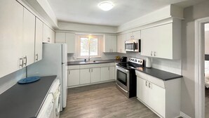 A modern kitchen with white cabinets, a stainless steel oven, a microwave, and a dishwasher. - Mountain View Suite - Sleeps 6
 (St. Catharines)