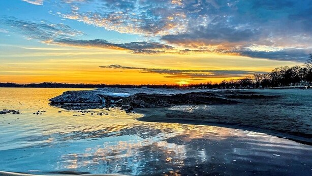 A frozen lake with a sunset in the background, a rocky shoreline, and a forested area. - Mountain View Suite - Sleeps 6
 (St. Catharines)