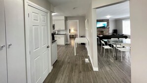 A modern kitchen with white cabinets, a dining area with a table and chairs, and a living room with a TV and seating. - Mountain View Suite - Sleeps 6
 (St. Catharines)