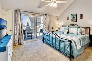 A bedroom with a bed, a TV, a ceiling fan, and a view of a building through a glass door.