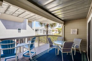 A covered outdoor deck with a table and chairs, a palm tree, and a sign on the wall. - Pelican Pointe 2C (Indian Shores)