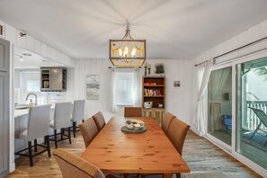A dining area with a wooden table, chairs, a chandelier, and a view of the outdoors. - Pelican Pointe 2C (Indian Shores)
