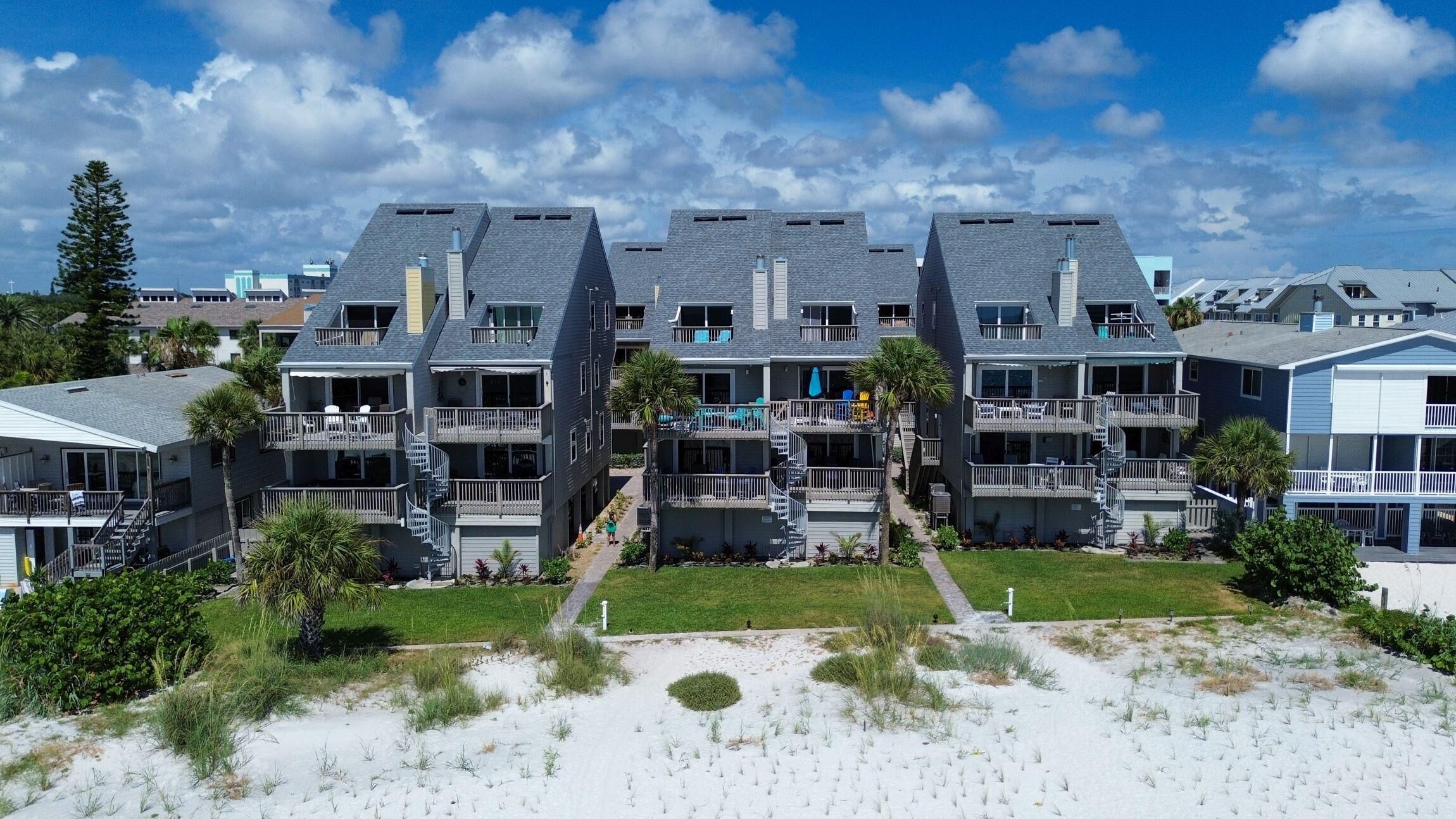 A beachfront hotel with multiple-story buildings, balconies, and a sandy beach area.