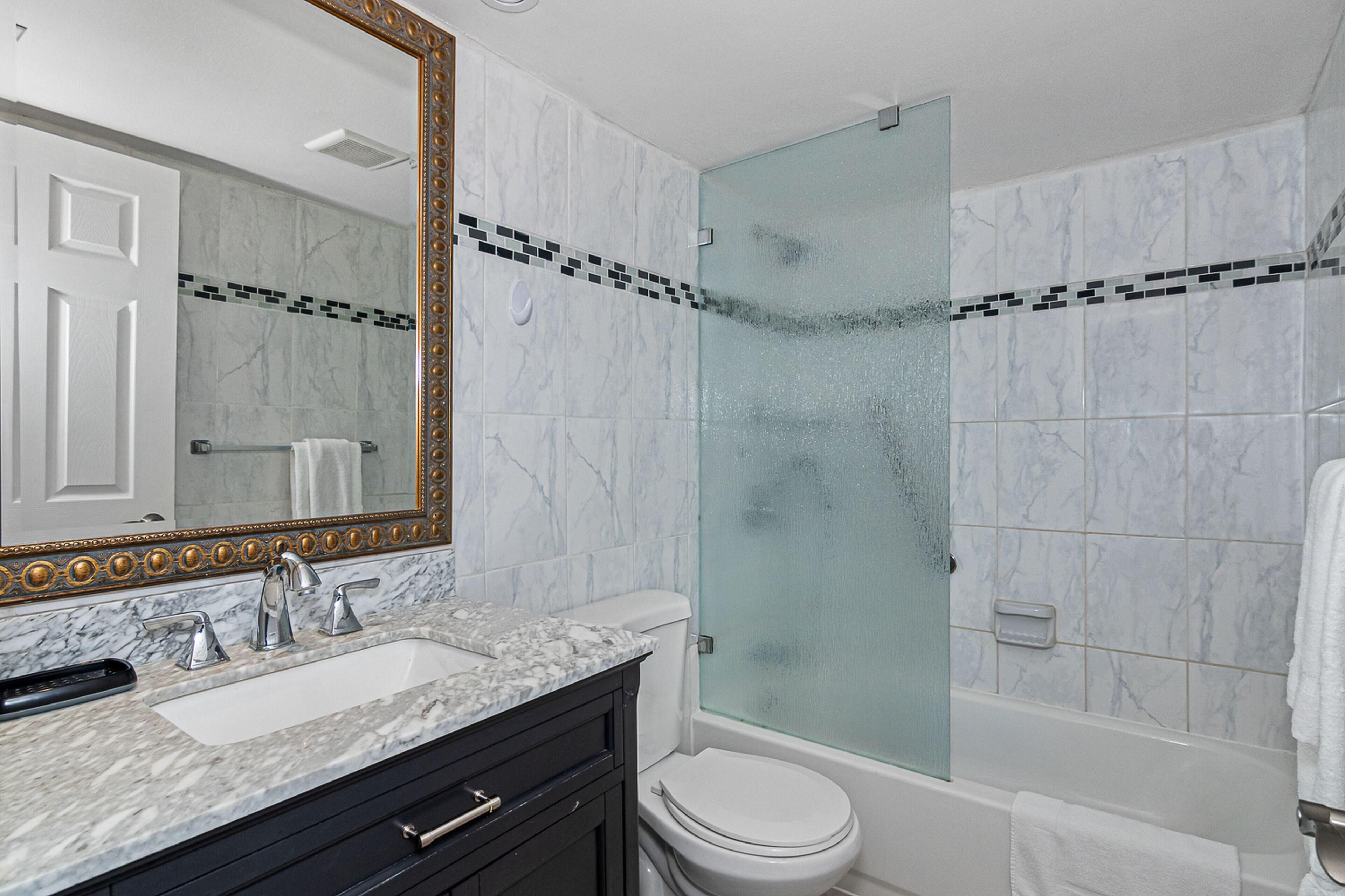 A bathroom with a marble sink, a large mirror, a glass shower enclosure, and a toilet.