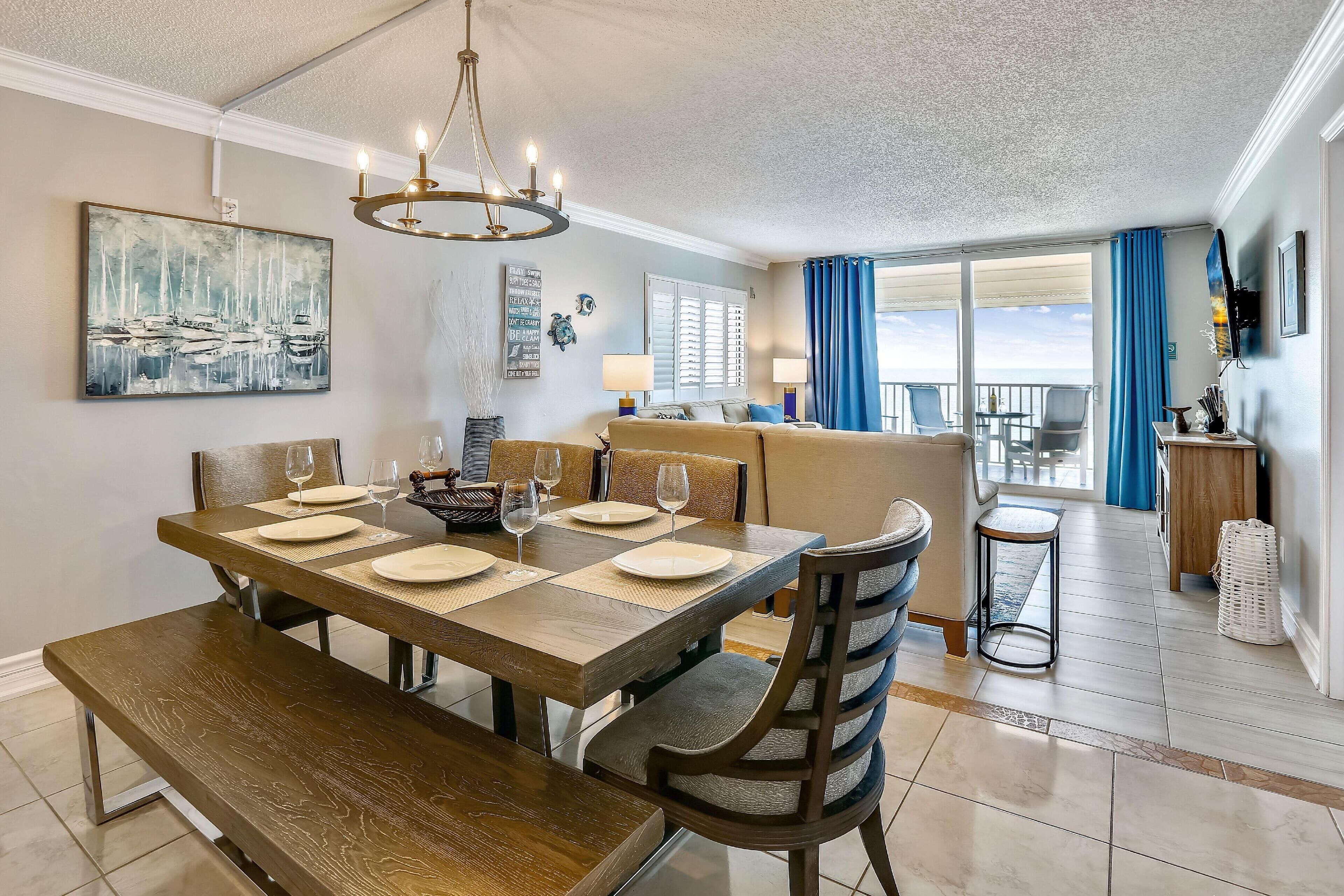 Un comedor con mesa de madera dispuesta para cuatro, una araña y vistas al exterior.