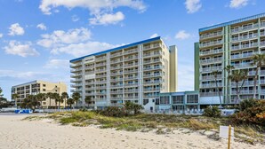 A beachfront hotel with multiple floors, balconies, and a sandy beach in the foreground. - Sand Castle 2703 (Indian Shores)