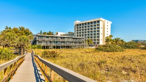 Une promenade en bois mène à un hôtel à étages, doté de nombreux balcons et entouré d’une végétation luxuriante.