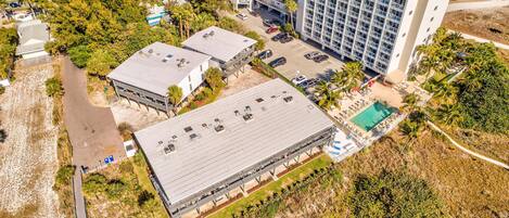 An aerial view of a hotel with a large parking lot, multiple buildings, and a pool area.