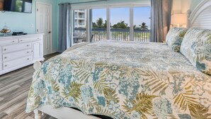 Een slaapkamer met een groot bed, een dressoir, een televisie en een balkon met uitzicht op palmbomen.