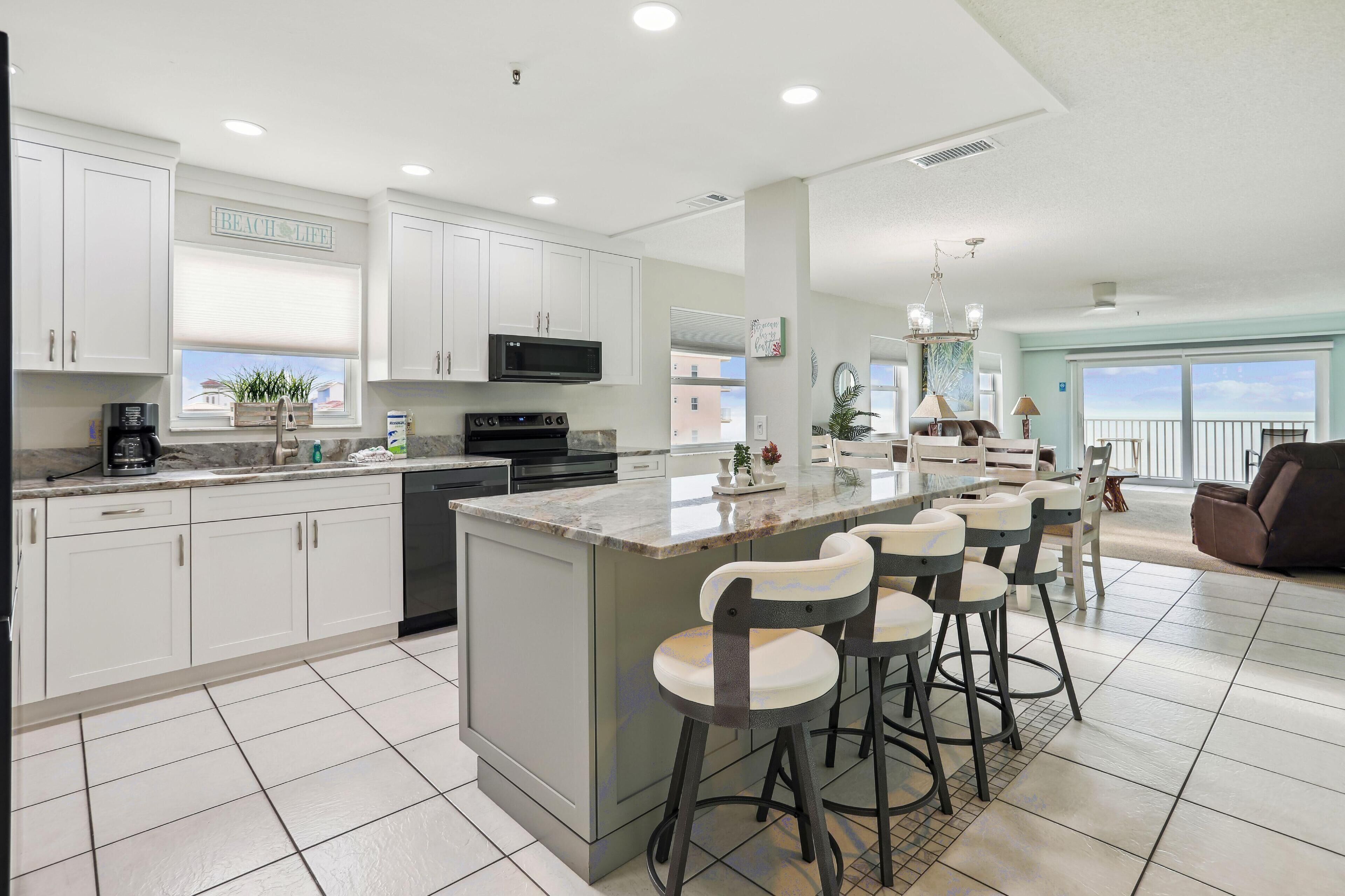 A modern kitchen with white cabinets, a large island with bar stools, and a view of the ocean.