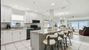 Una cocina moderna con armarios blancos, una isla grande con taburetes de bar y vistas al océano.