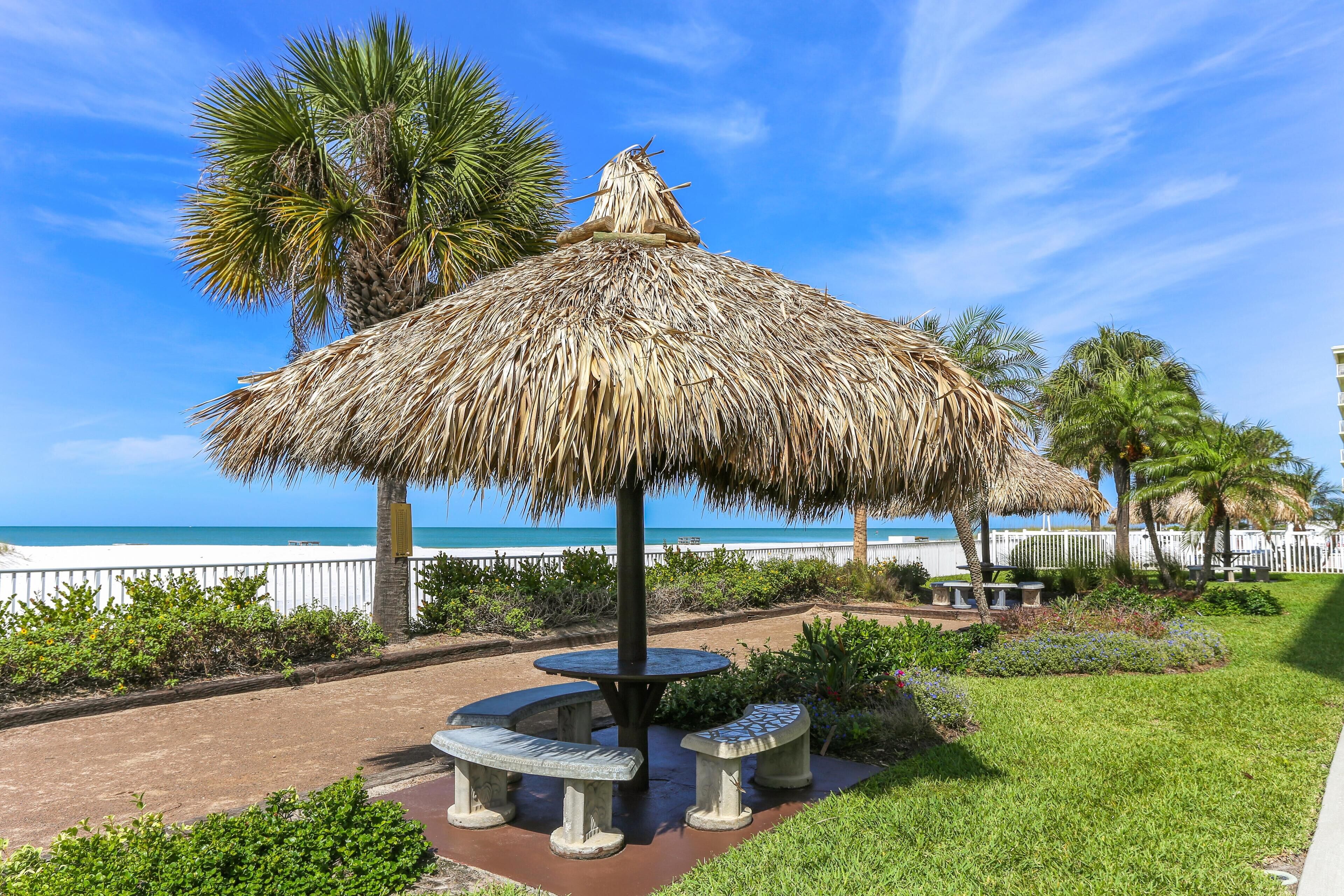 A thatched umbrella structure with benches, palm trees, and a view of the ocean.