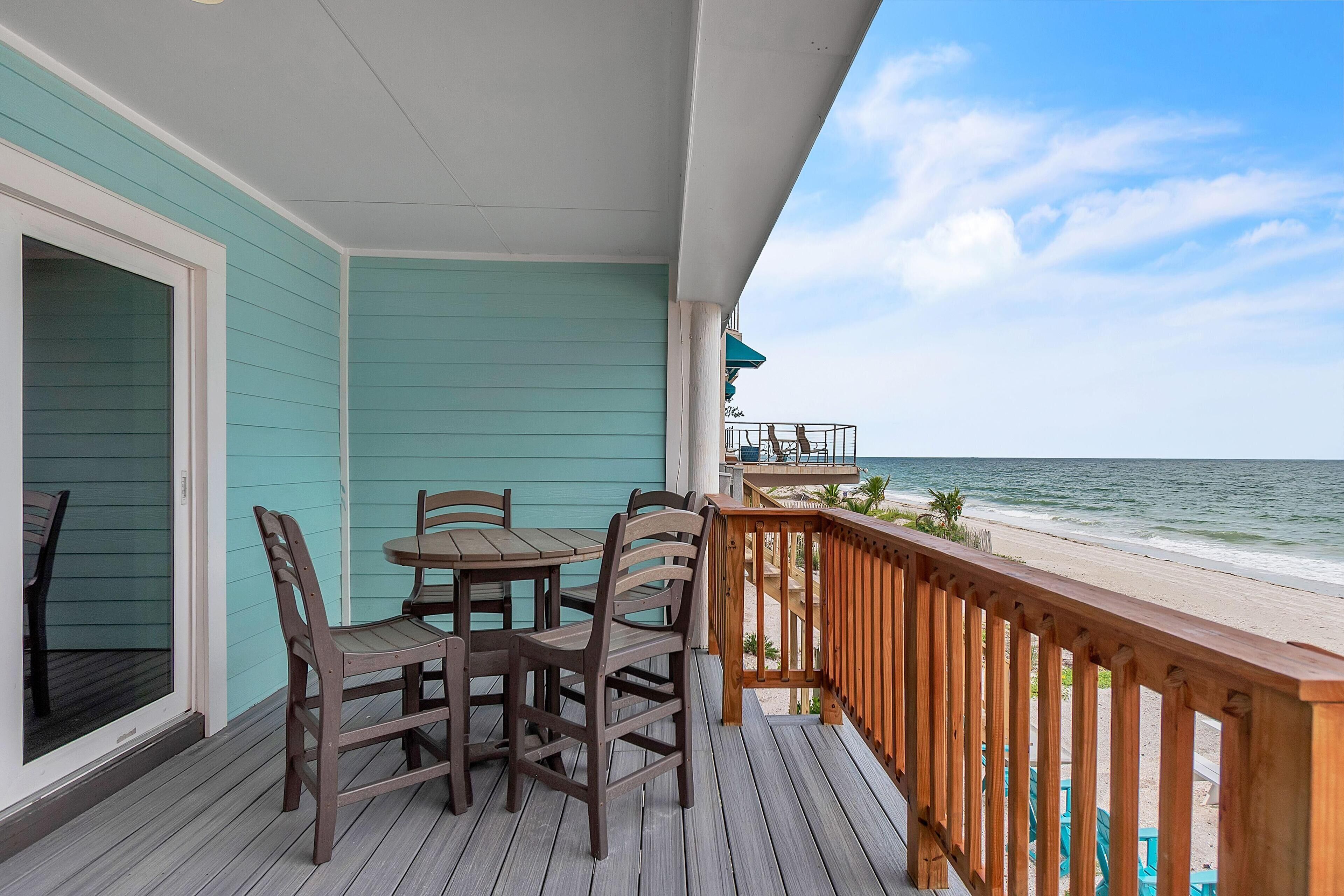 A wooden deck with a table and chairs, overlooking a beach with a wooden railing.