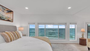 A bedroom with a large bed, a view of the ocean, and a painting on the wall. - Serenity By The Sea (Treasure Island)