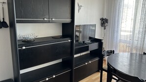 A modern kitchen with black cabinetry, a dining table, and a large window with sheer curtains. - Appartement Les Lupins vue Port (Courseulles-sur-Mer)