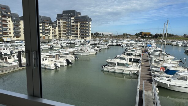 A marina with numerous boats docked, surrounded by multi-story buildings. - Appartement Les Lupins vue Port (Courseulles-sur-Mer)