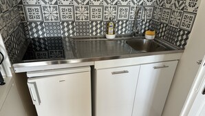 A compact kitchen with a stainless steel sink, a white refrigerator, and a patterned backsplash. - Appartement Les Lupins vue Port (Courseulles-sur-Mer)
