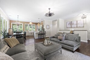 Un salon spacieux avec un canapé gris, un pouf et un coin repas comprenant une table et des chaises.