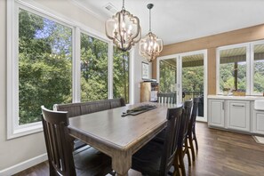 Un espace repas avec une grande table en bois, des chaises sombres et des luminaires suspendus.