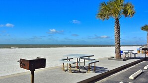 Een picknickplaats aan het strand met tafels en banken, een palmboom en uitzicht op de oceaan.