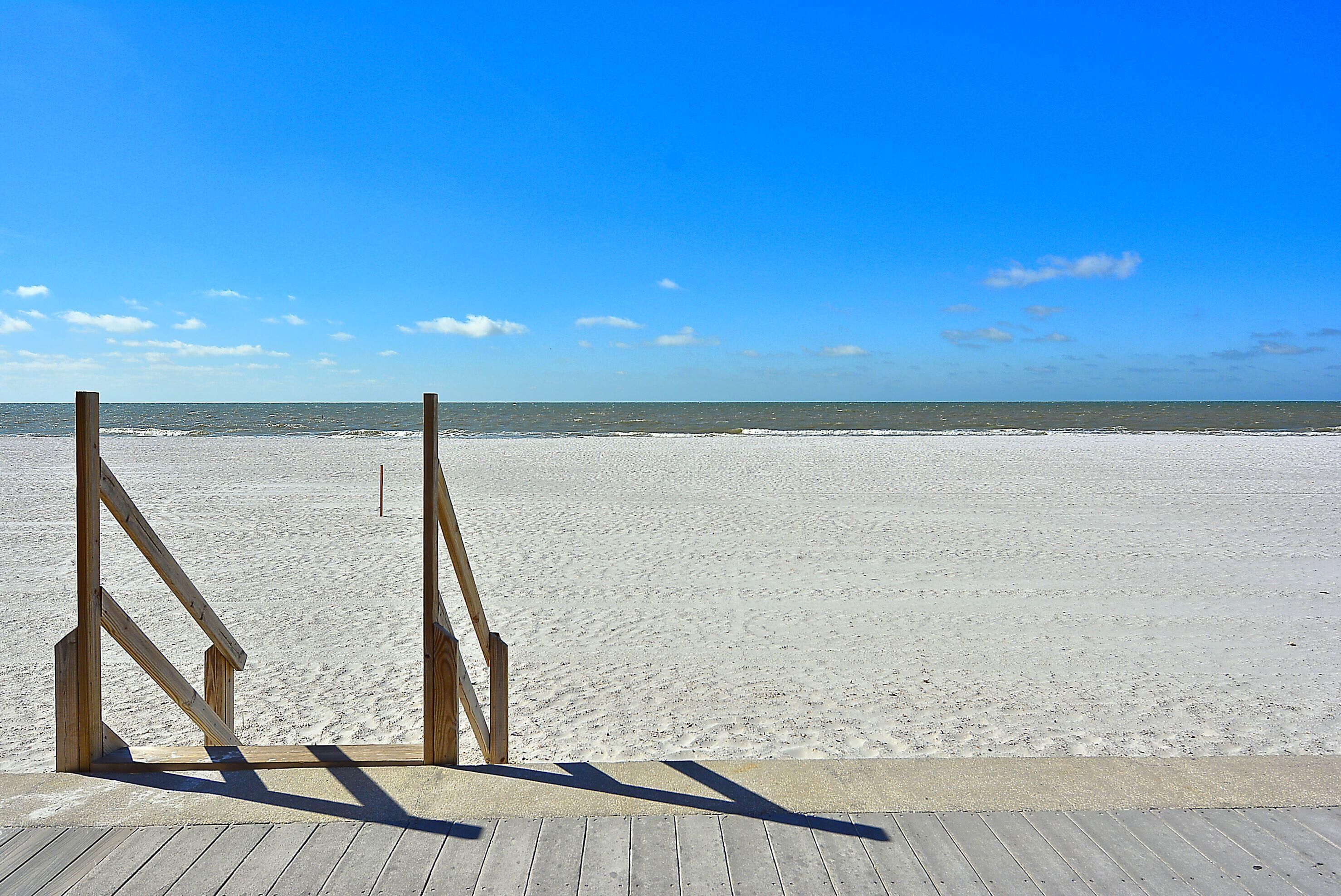 A wooden boardwalk leading to a sandy beach with a clear blue sky.