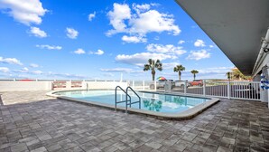 Une piscine avec vue sur l’océan et des palmiers, le tout sous un ciel dégagé.