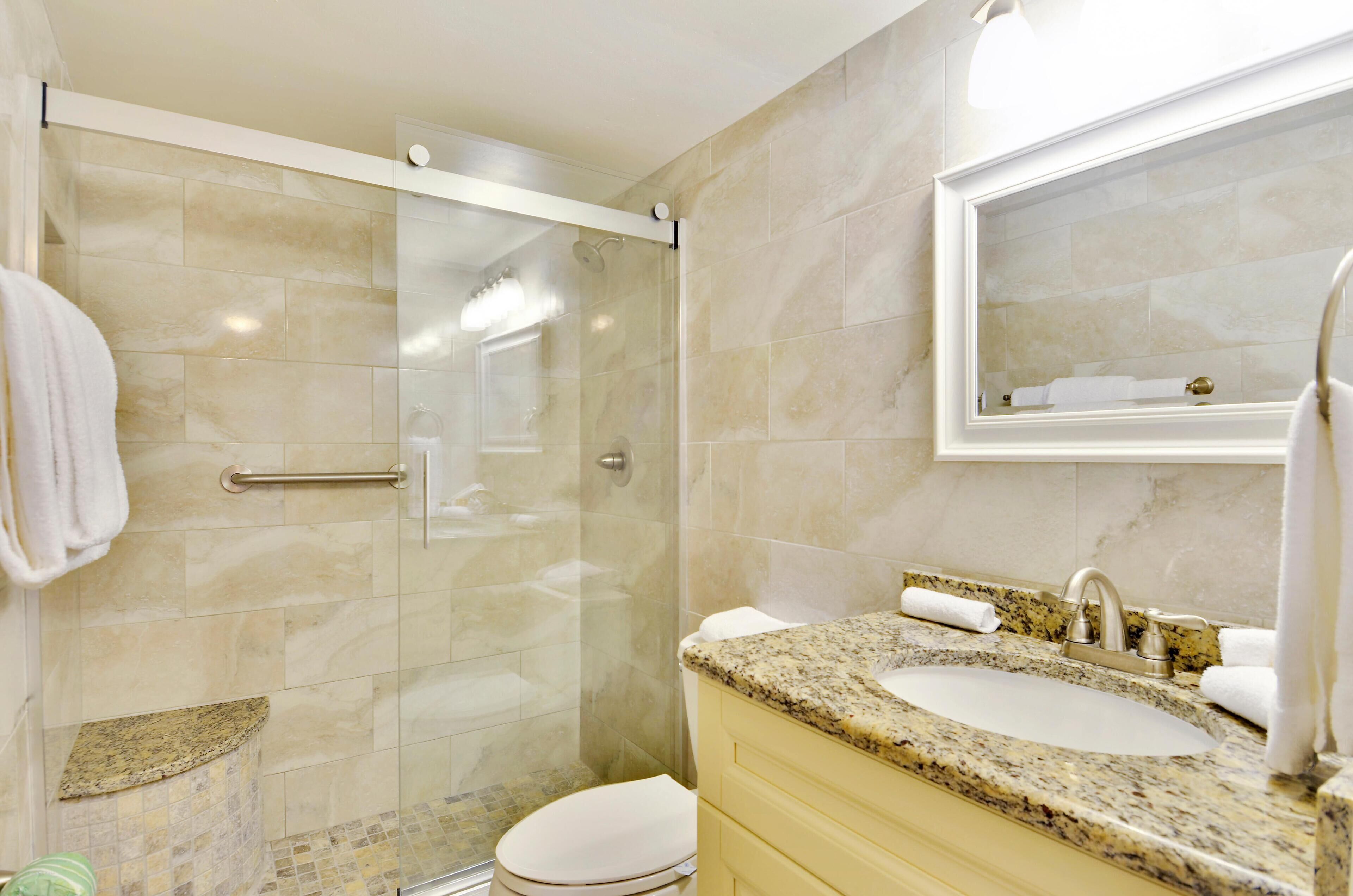 Une salle de bain moderne avec une douche à parois de verre, un lavabo sur un plan de travail en granit et un grand miroir au-dessus du meuble-lavabo.