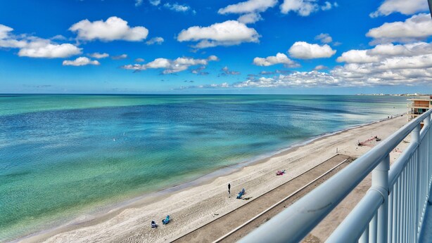 Une plage à l’eau turquoise et limpide, un rivage sablonneux et quelques personnes.