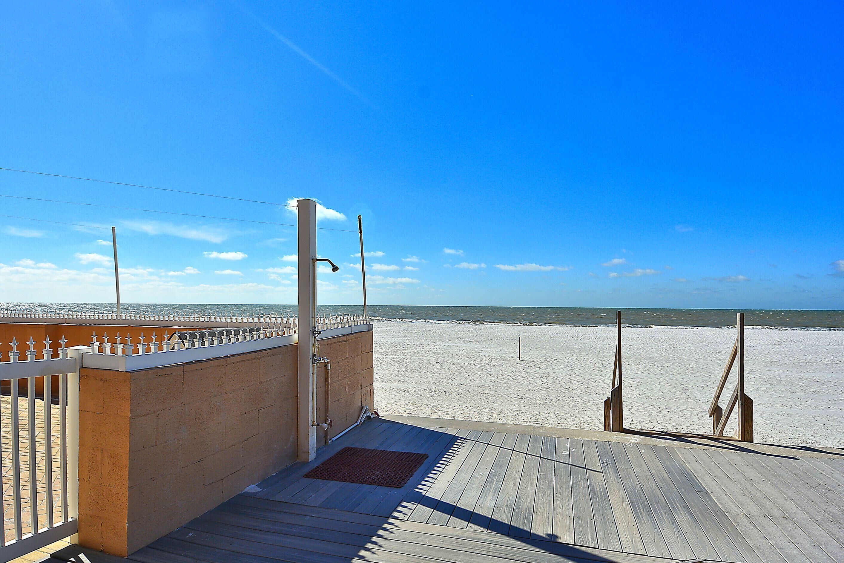 A wooden deck leading to a beach with a clear sky.