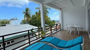 A balcony with blue lounge chairs, a small table, and chairs, overlooking a beach and palm trees. - Raalhu Fonu Maldives  (Mahibadhoo)