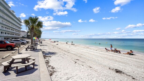 A beach with a wooden walkway, picnic tables, and umbrellas. - Sunset Chateau 611 (Treasure Island)