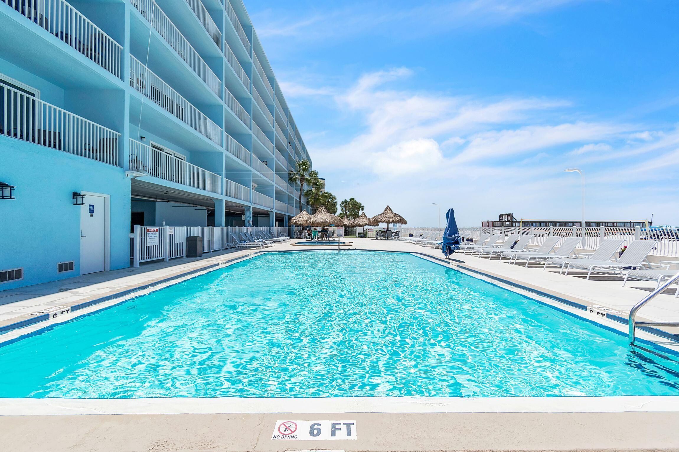 A swimming pool with a no diving sign, a building with balconies, and a clear sky.