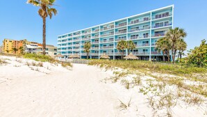 A beachfront hotel with multiple balconies, a sandy beach, and palm trees.