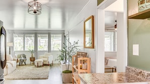 A modern living room with a large window, a sofa, a coffee table, and a potted plant. - Hilo Apartment w/ Lanai - 2 Mi to Beaches! (Hilo)