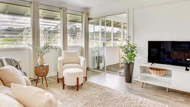 A modern living room with a large TV, comfortable seating, and large windows offering a view of the outdoors. - Hilo Apartment w/ Lanai - 2 Mi to Beaches! (Hilo)