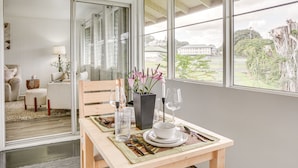 A dining area with a table set for two, a vase with flowers, and a view of the outdoors. - Hilo Apartment w/ Lanai - 2 Mi to Beaches! (Hilo)