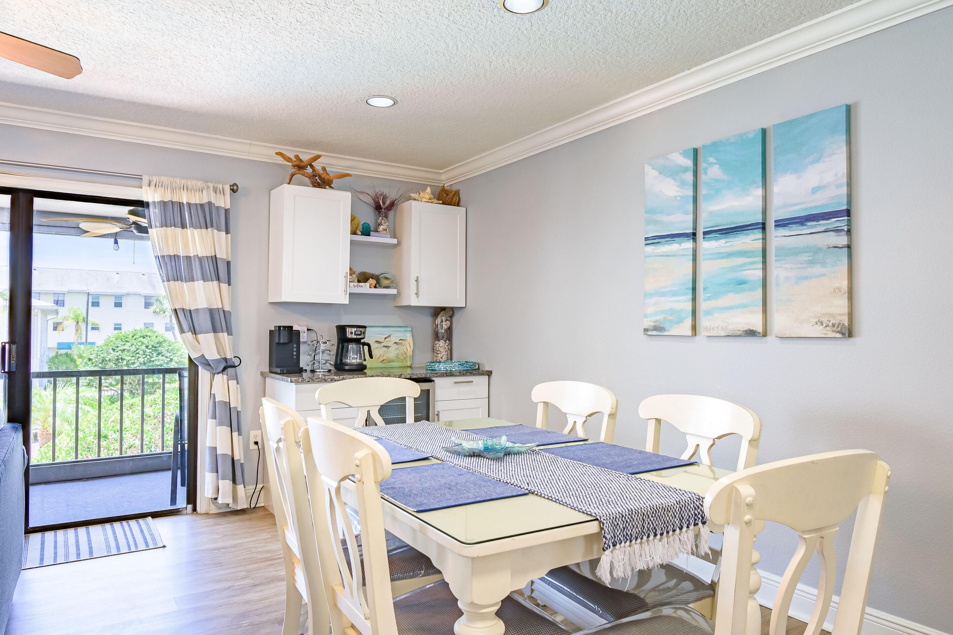 A dining area with a table set for four, white chairs, and a view of the outdoors through a glass door.
