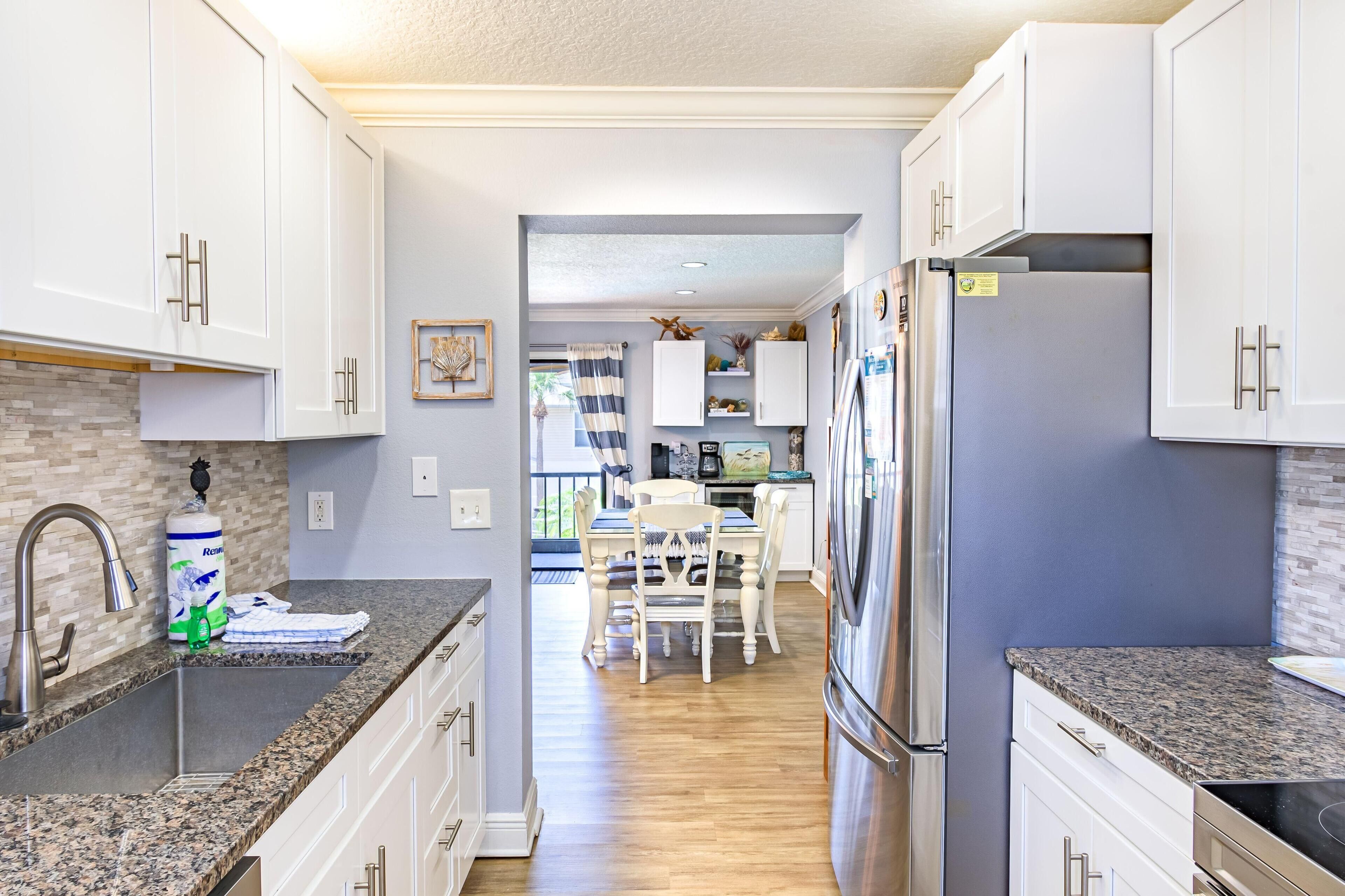 Una cocina moderna con armarios blancos, encimeras de granito, electrodomésticos de acero inoxidable y una zona de comedor con mesa y sillas.