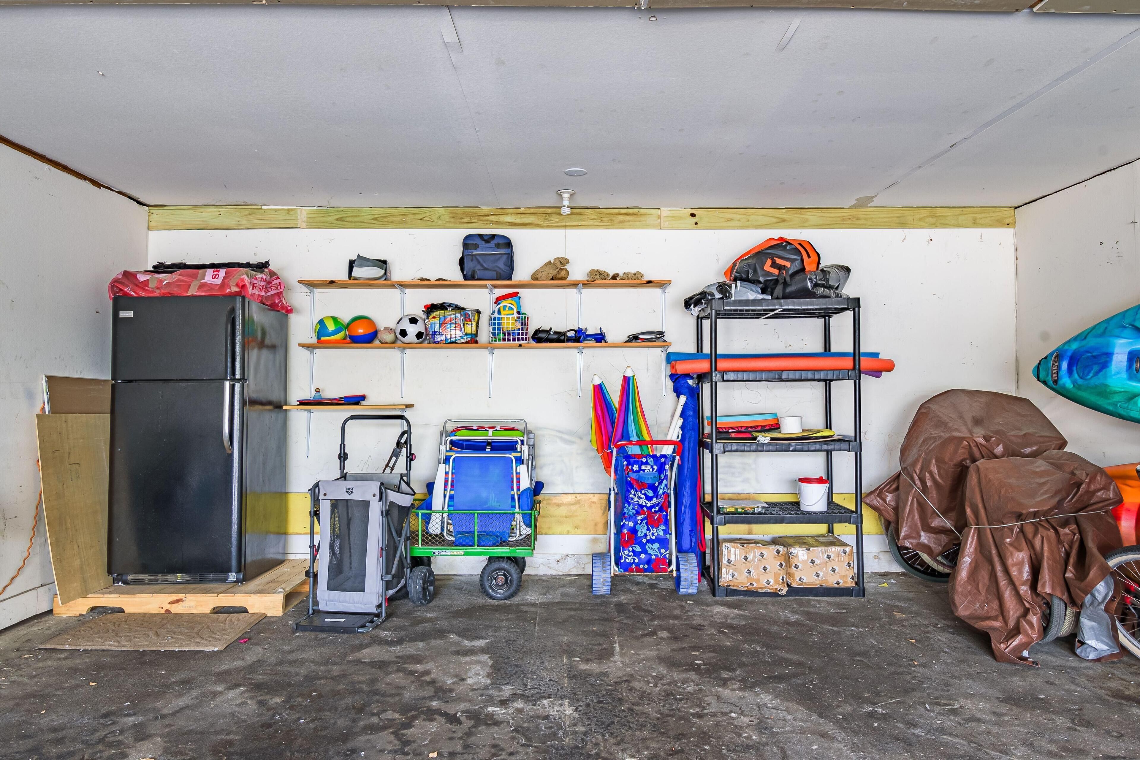 Un garage con frigorifero, un carrello, scaffali con attrezzatura sportiva e una bicicletta al coperto.
