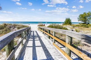 A wooden boardwalk leading to a beach with clear skies and calm waters. - Sea Shell 14 - Premier (Indian Shores)