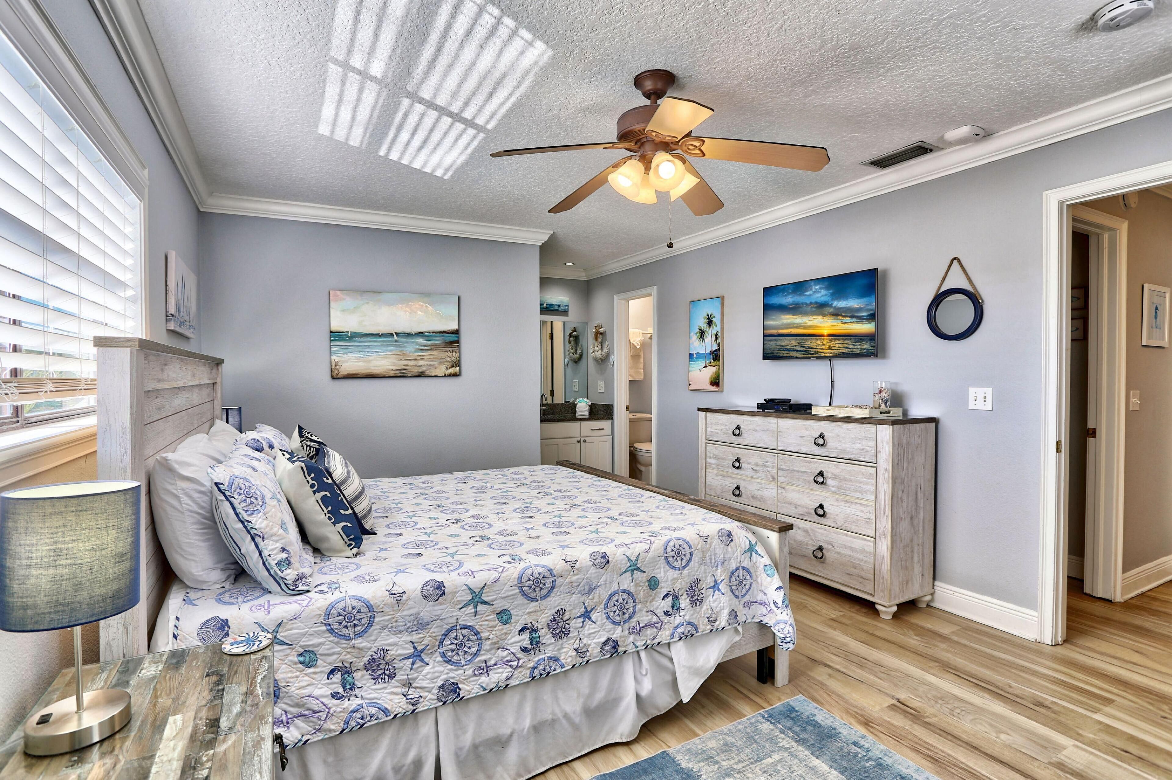 A bedroom with a bed, a ceiling fan, a dresser, and artwork on the walls.
