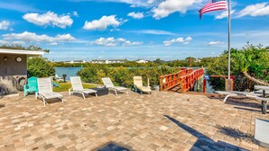 Une terrasse avec des chaises longues, un drapeau et une vue sur une étendue d ’eau et des bâtiments.