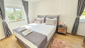 A modern bedroom with a large bed, grey bedding, a wooden nightstand, and a fluffy rug.