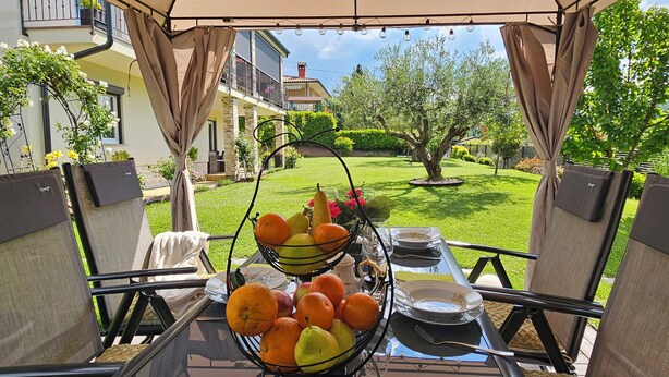 An outdoor dining area with a table set for two, surrounded by chairs, and a fruit basket on the table.
