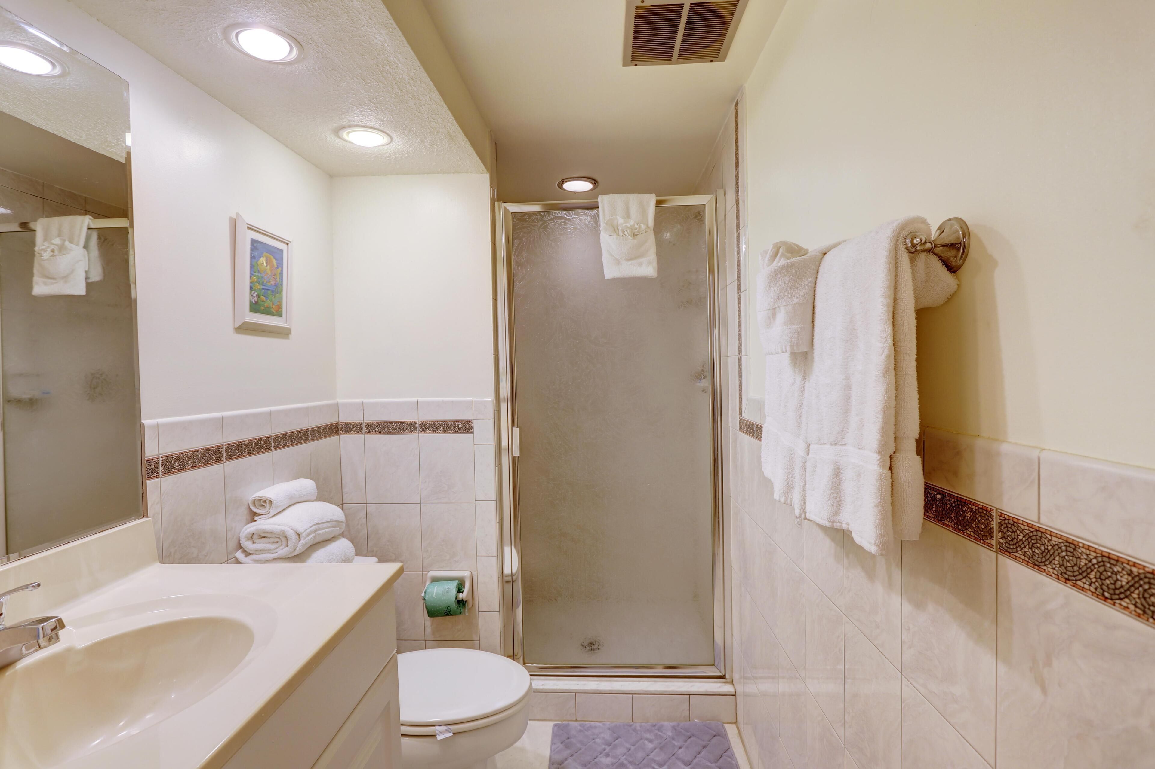 Ein Badezimmer mit Waschbecken, Toilette und Dusche. Handtücher hängen an der Wand und ein Bild ist aufgehängt.