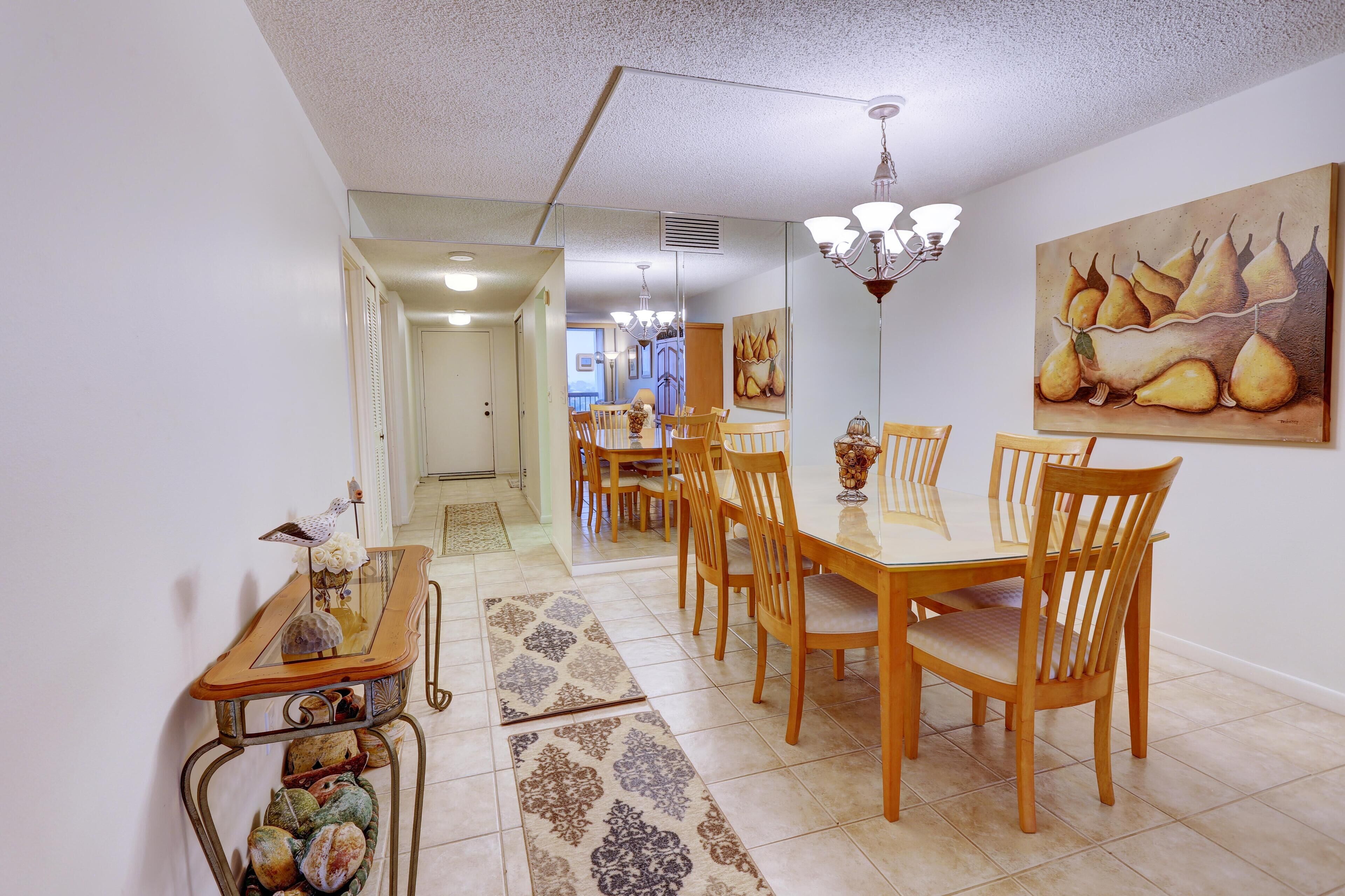 A dining area with a wooden table and chairs, a chandelier, and a painting of pears on the wall.