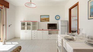 A modern kitchen with white cabinets, a dining table set for four, and a large window providing natural light.