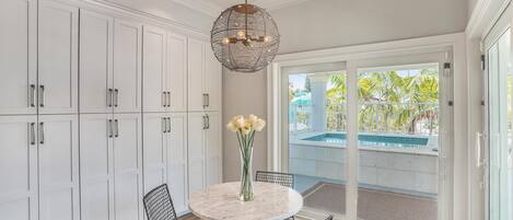 A kitchen with white cabinets, a round marble table, black wire chairs, and a hanging light fixture.