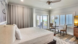 Camera d'albergo con un letto grande, un ventilatore a soffitto, vista sull'oceano, zona pranzo e televisione.